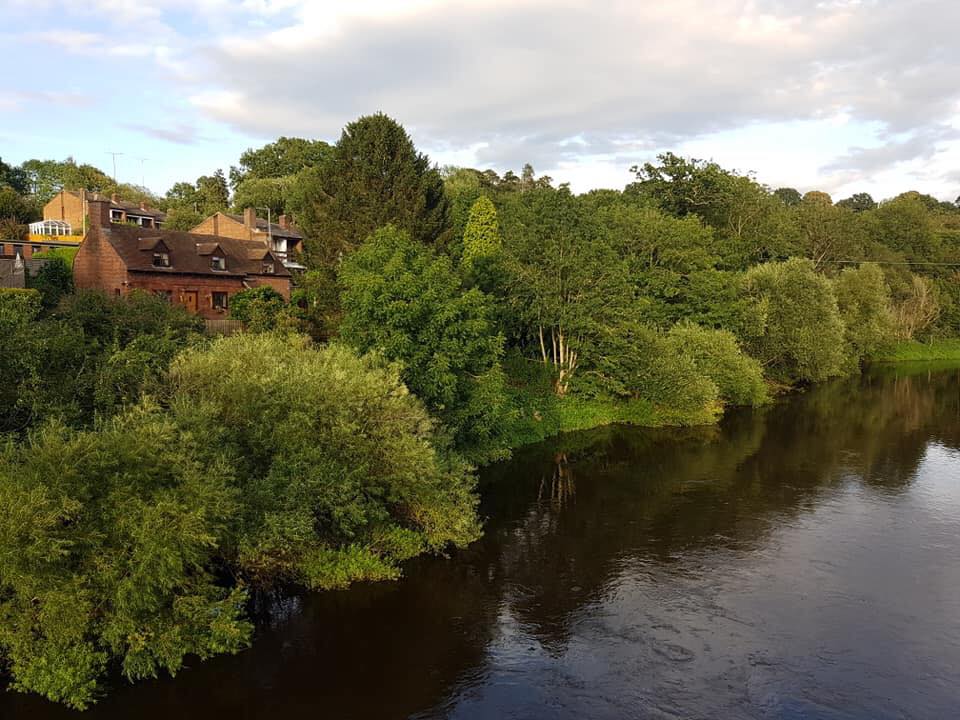 The river Severn as you head into Bewdley, on the far side the trees are in full green leaf and a few red brick houses are dotted around the woodland.